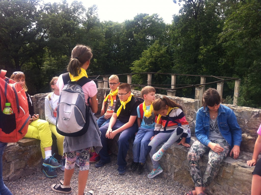 Dzieci w żółtych chustach z opiekunami siedzący na kamiennym murku