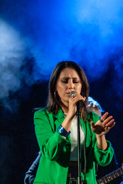 Kobieta w zielonej marynarce śpiewa na scenie