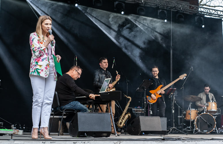 Na boku sceny śpiewa kobieta, w tle widać kapelę muzyczną