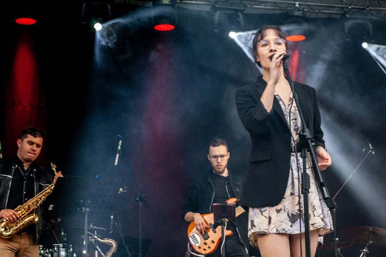 Kobieta w sukience śpiewa na scenie, w tle widać muzyków