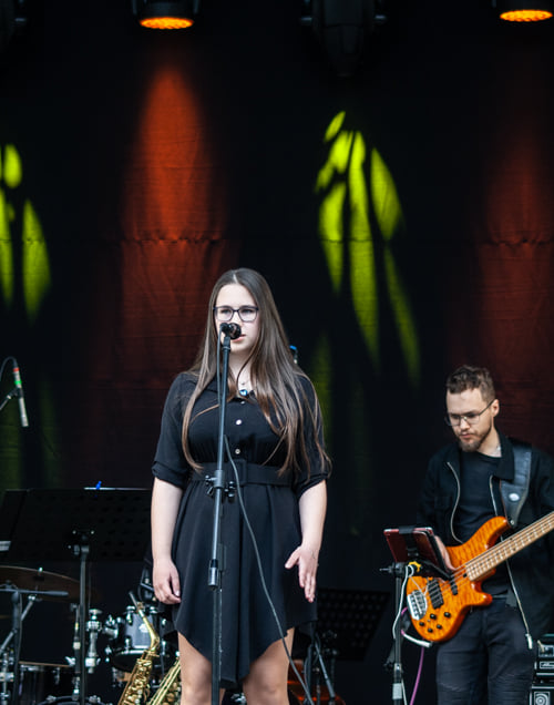 Kobieta w sukience śpiewa na scenie, w tle widać gitarzystę