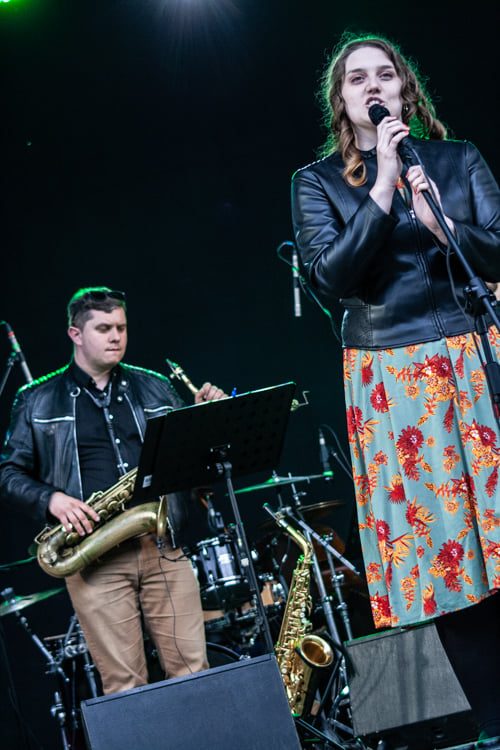 Kobieta w sukience śpiewa na scenie, w tle widać saksofonistę