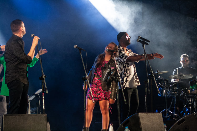 Na zdjęciu widać trzech wokalistów, w tle znajduje się perkusista