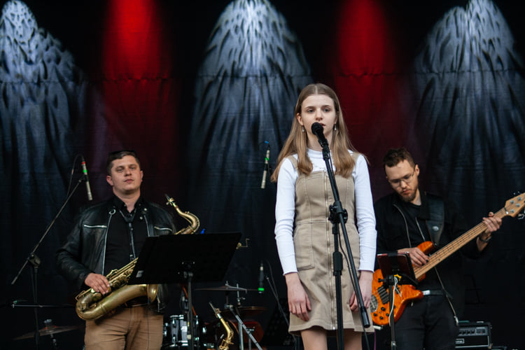 Na środku sceny śpiewa kobieta, w tle widać muzyków