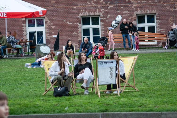 Zdjęcie przedstawia kobiety siedzące na leżakach, w tle widać ludzi