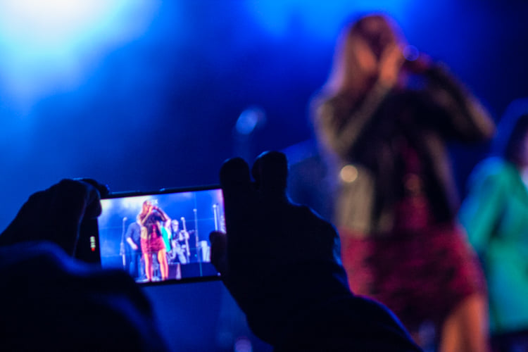 Zdjęcie przedstawia osobę nagrywającą koncert telefonem