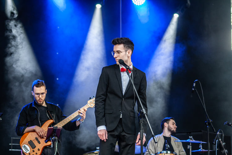 Mężczyzna śpiewa na scenie, w tle widać muzyków