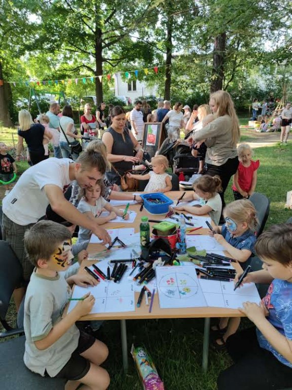 Dzieci z opiekunami wykonujące prace plastyczne w parku