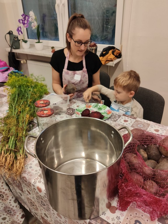 Kobieta ucząca małego chłopca jak kroić warzywa, na stoliku duży garnek
