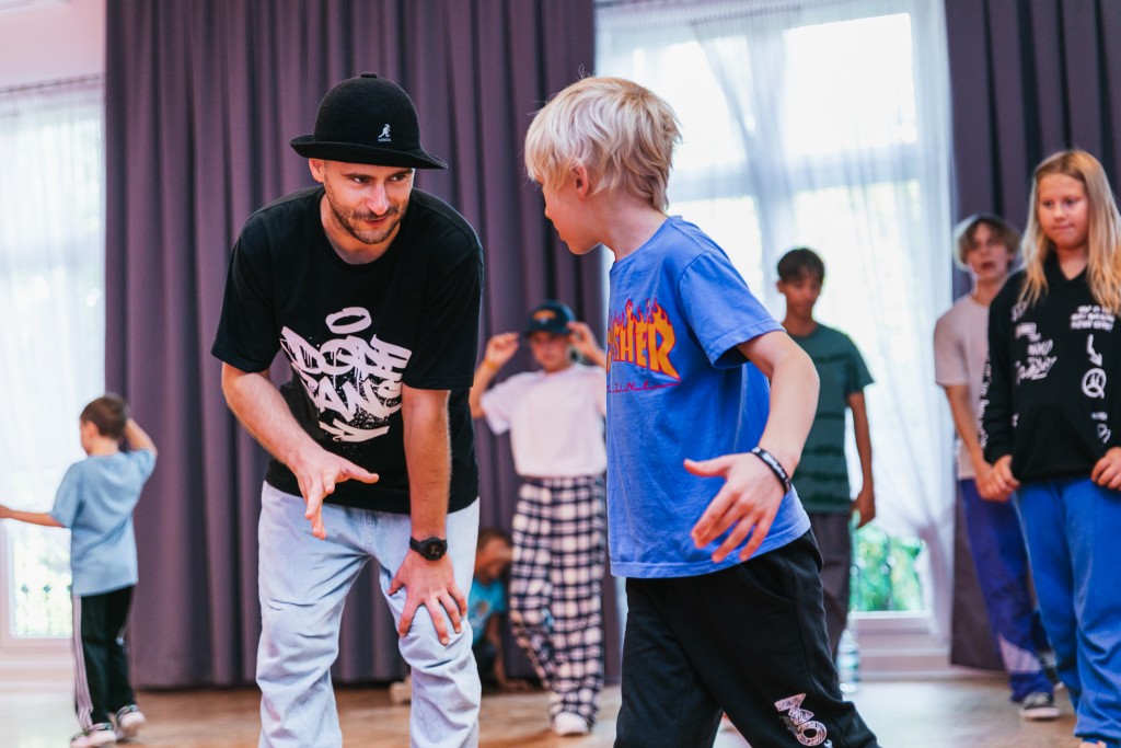 Mężczyzna uczy chłopca ruchów tanecznych, za nimi inne dzieci