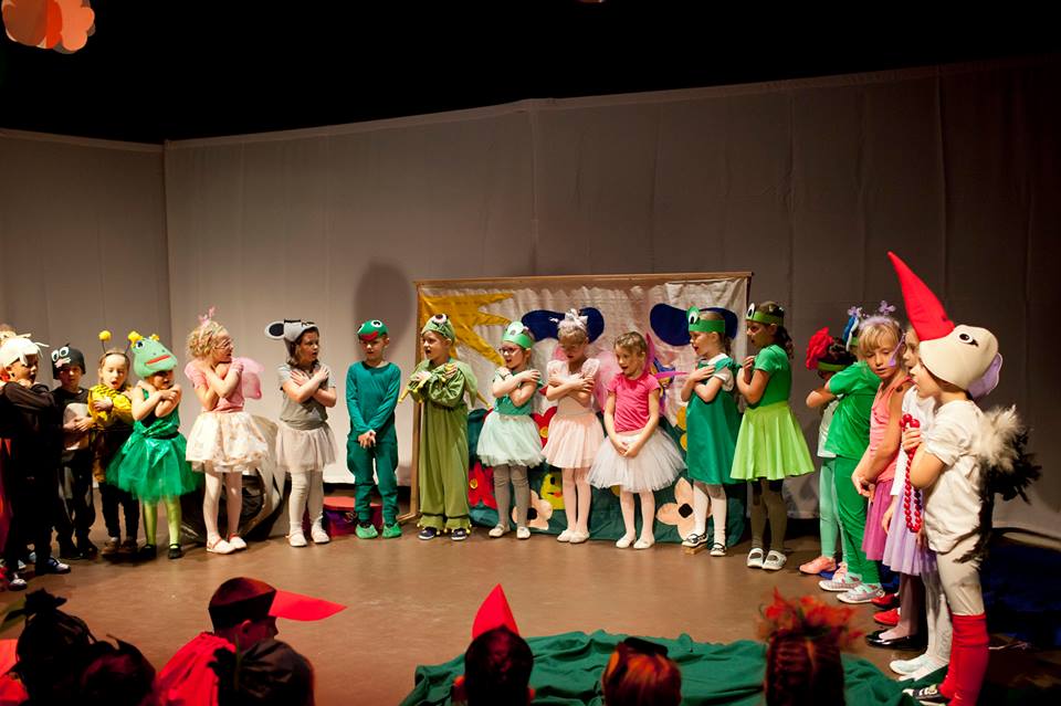 Kolorowo poubierane dzieci stoją obok siebie na scenie