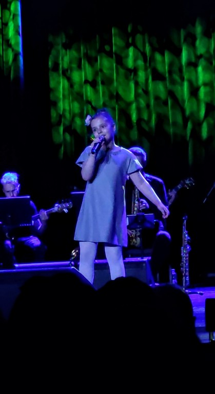 Dziewczynka w szarej sukience śpiewa na scenie