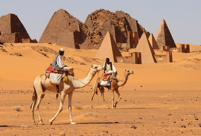 Dwójka ludzi na wielbłądach idących przez pustynie pełną piramid