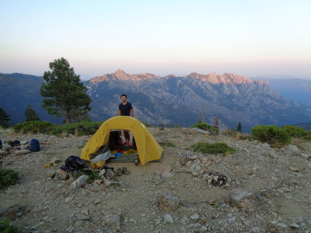 Osoba stojąca za żółtym namiotem postawionym na wzgórzu, w tle góry
