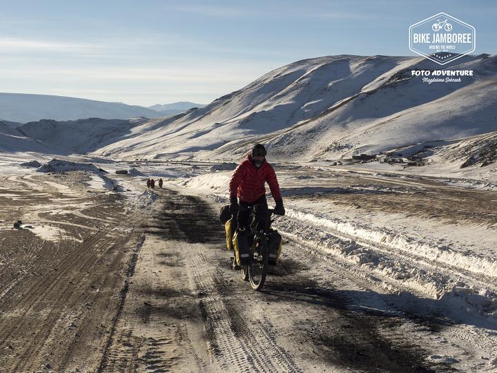 Osoba w kurtce jadąca na rowerze przez wzgórzysty, śnieżny teren