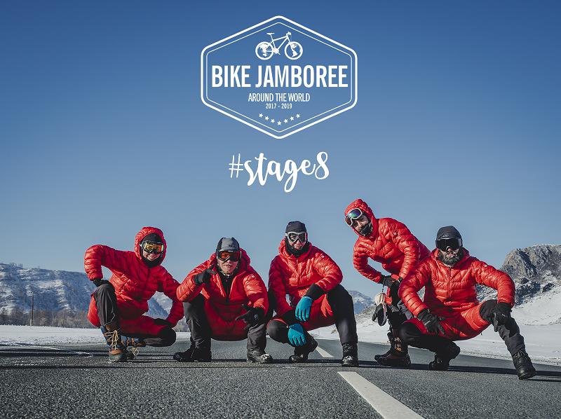 Grupa ludzi w czerwonych kurtkach stoi na drodze, nad nimi logo 'Bike Jamboree' i napis '#stages'