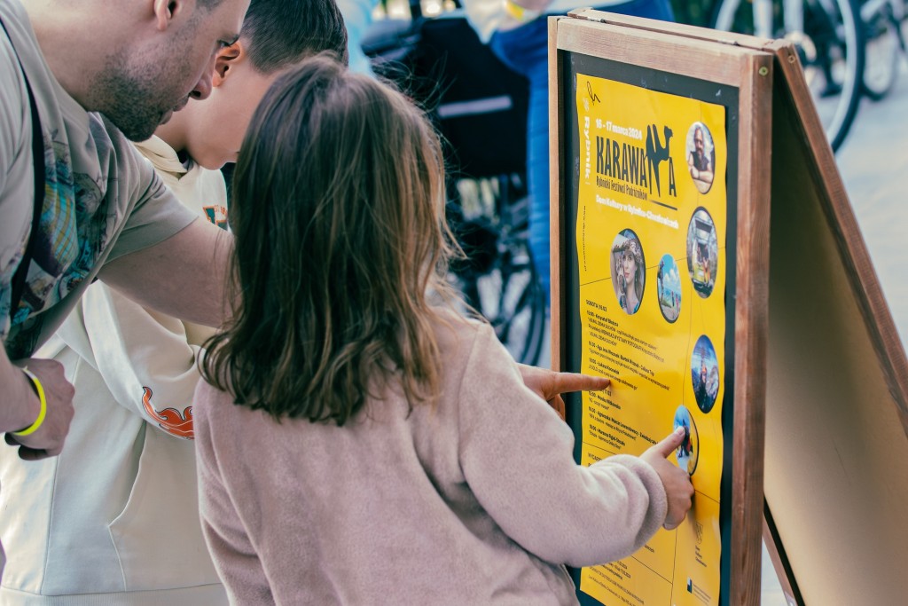 Mężczyzna pokazuje dwójce dzieci plakat festiwalu 