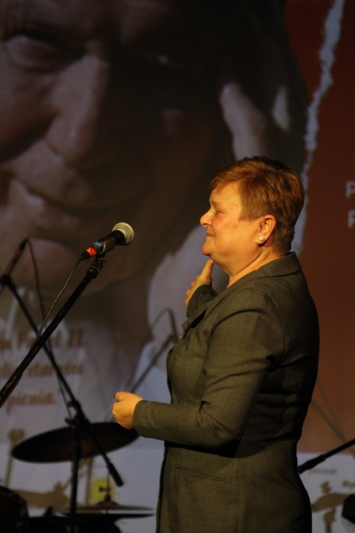 Kobieta zwraca się do publiczności ze sceny.
