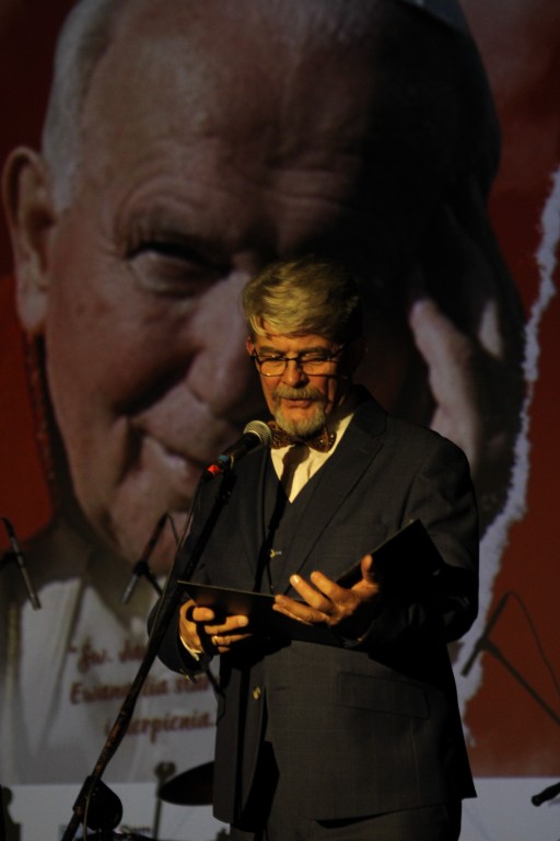 Konferansjer podczas koncertu, w tle wizerunek Jana Pawła II