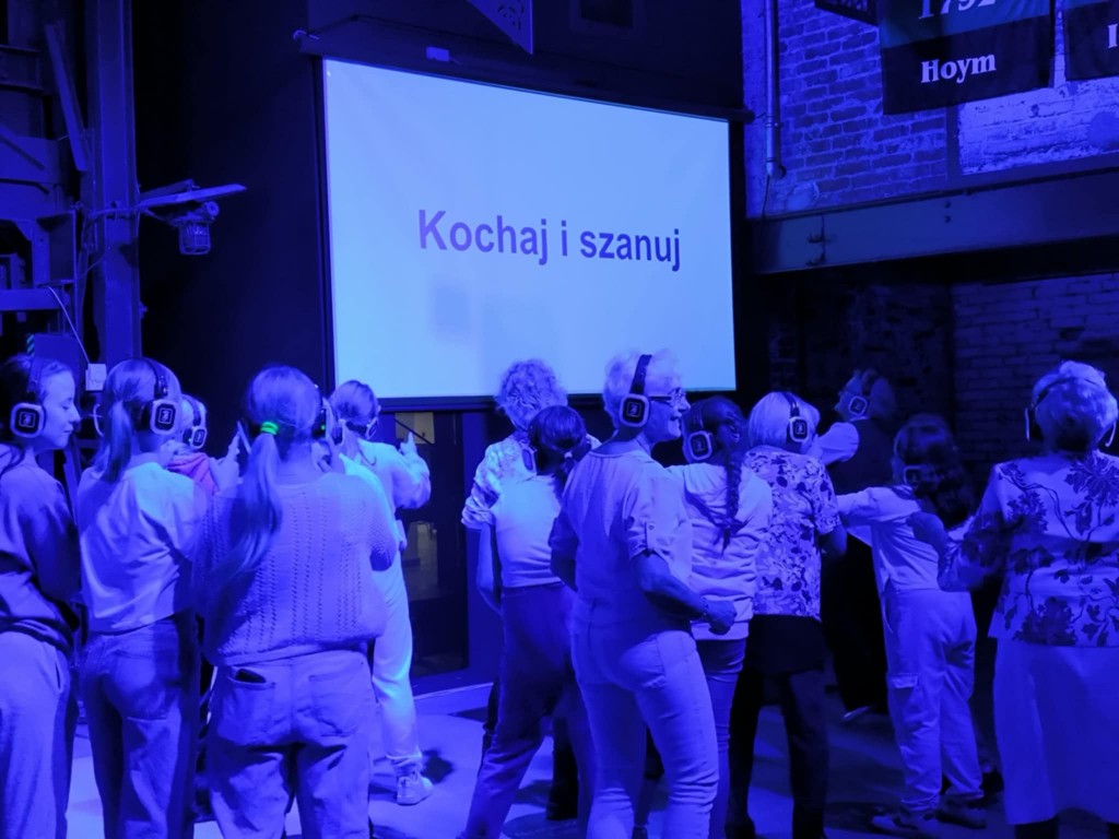 grupa osób tańczy, w tle na ekranie hasło kochaj i szanuj