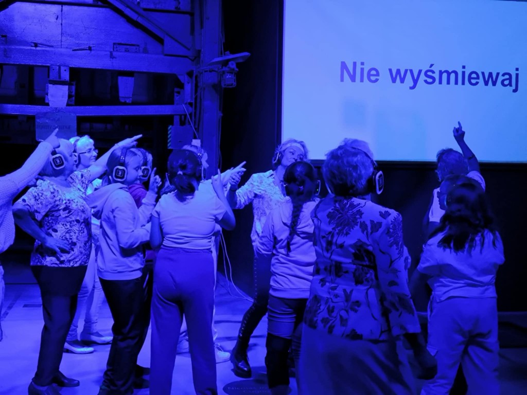 grupa osób tańczy, w tle na ekranie hasło: nie wyśmiewaj
