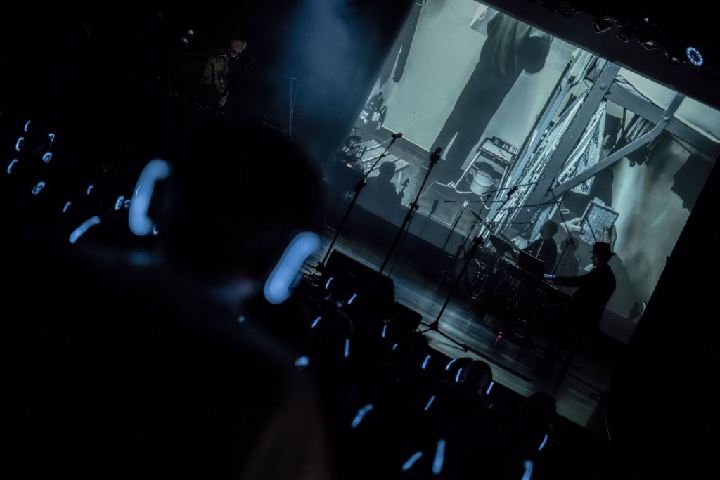 widok na scenę z widowni, na scenie muzycy a w tle ekran z kadrem z filmu