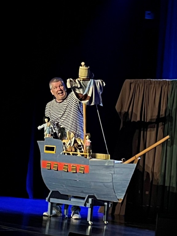 występ sceniczny, mężczyzna w koszuli w paski, teatr lalek, na scenie statek piracki