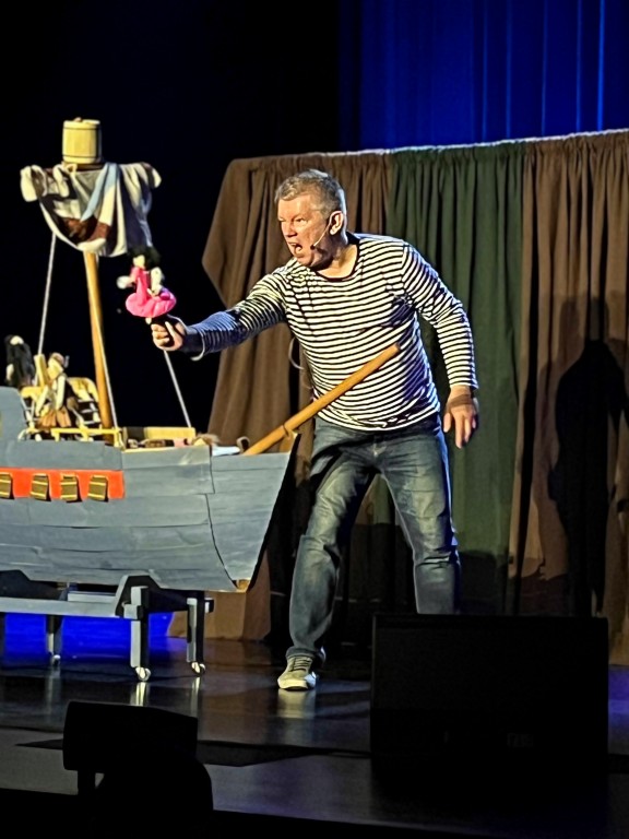 występ sceniczny, mężczyzna w koszuli w paski, teatr lalek, na scenie statek piracki