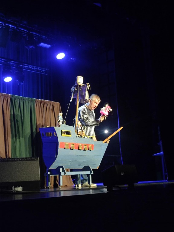 występ sceniczny, mężczyzna w koszuli w paski, teatr lalek, na scenie statek piracki
