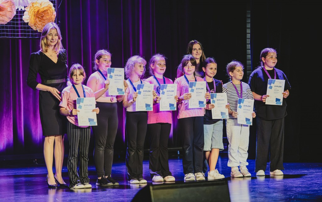Dziewczynki w różowych bluzkach stoją na scenie z dyplomami i medalami.