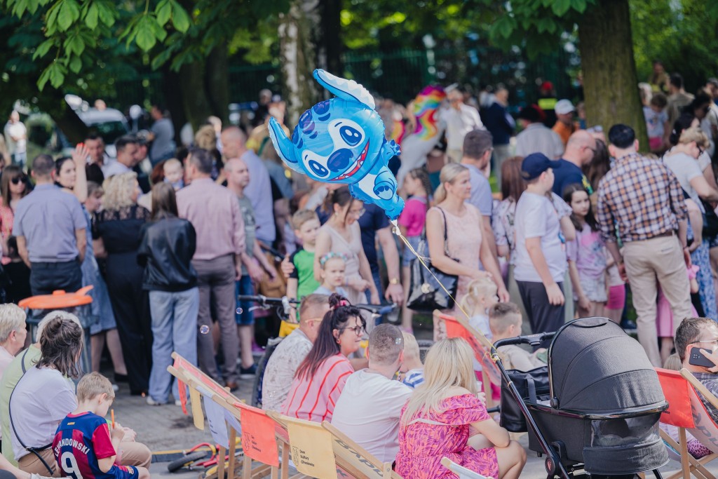 Tłum ludzi w parku; niektórzy trzymają duże balony w kształcie postaci z filmów animowanych.