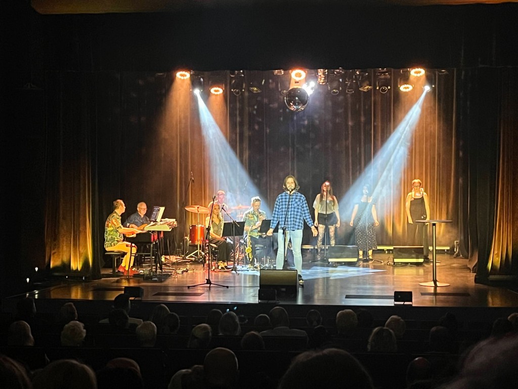 Publiczność ogląda koncert na scenie oświetlonej ciepłym światłem reflektorów.