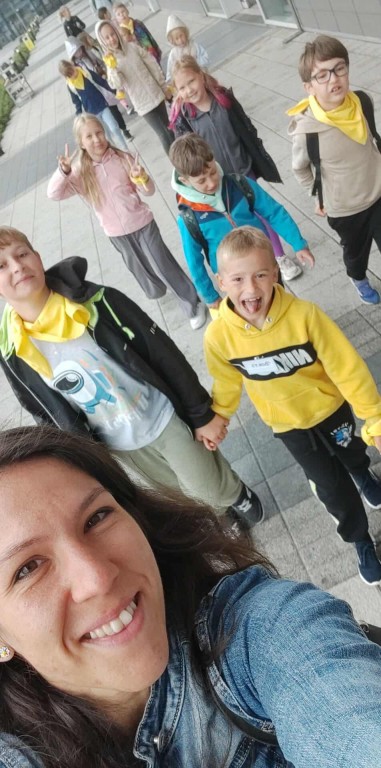 Grupa dzieci idzie wraz z Panią wychowawczynią na wycieczce.