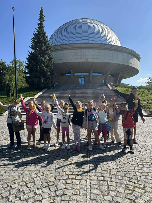 Dzieci stoją przed planetarium i machają.