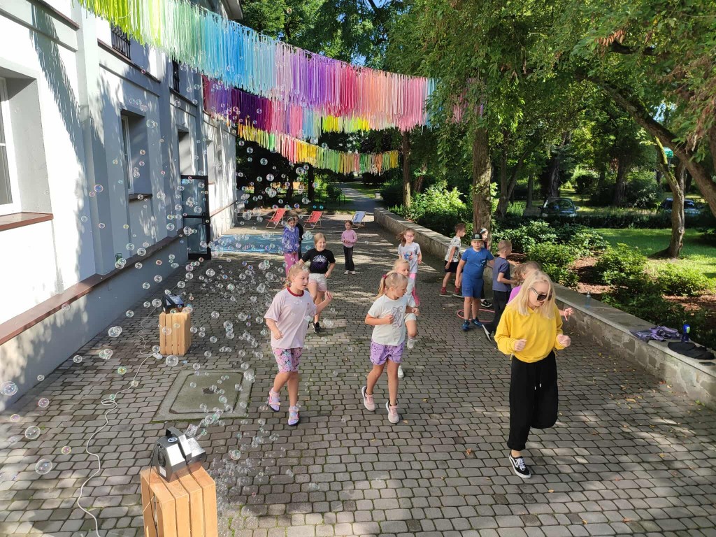 Dzieci tańczą na dworze z opiekunką.