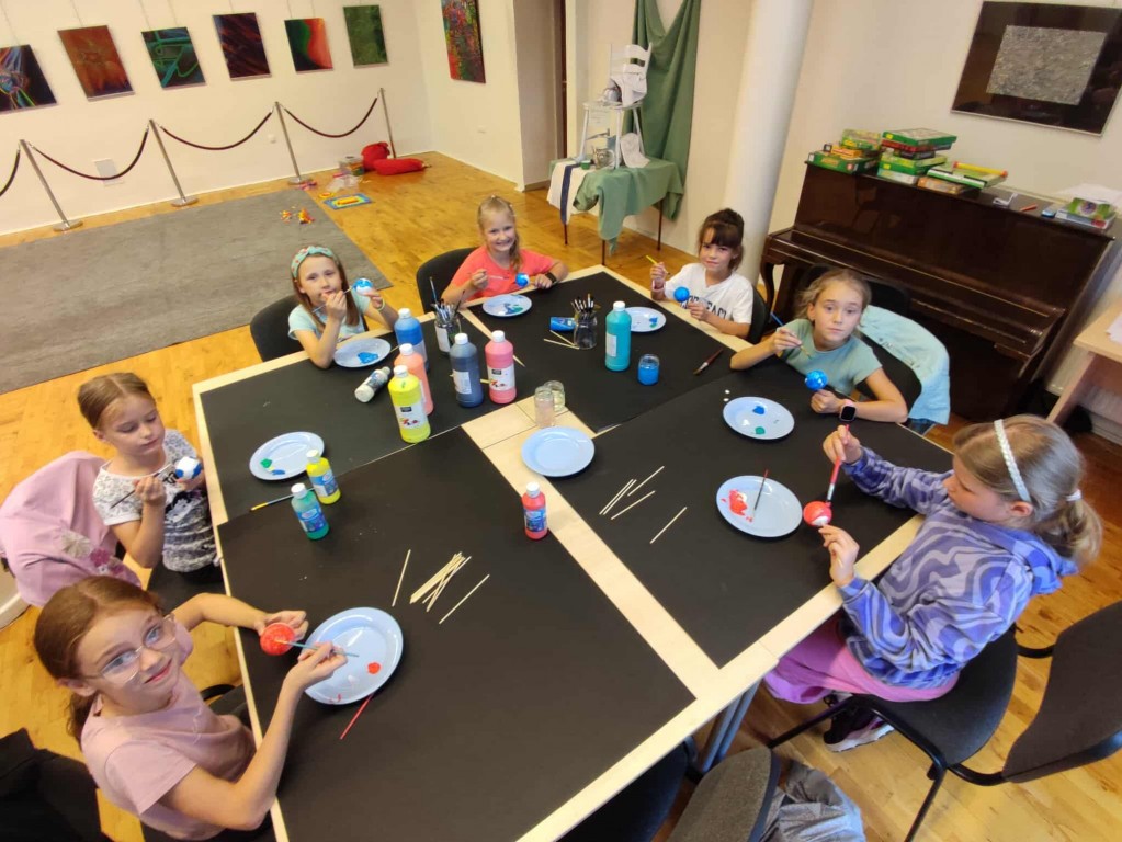 Dziewczynki siedzą przy stole i malują farbami.