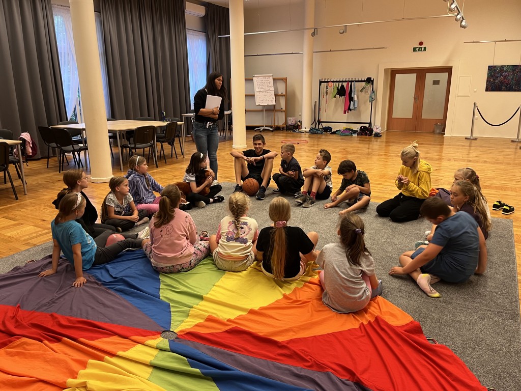 Dzieci siedzą w kółku i słuchają opiekunki.