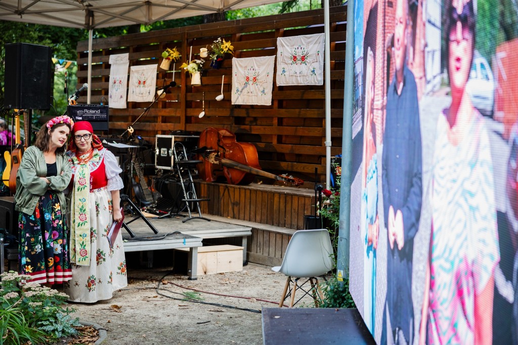 Dwie kobiety przed sceną patrzą na ekran, jedna z kobiet ubrana w tradycyjny śląski strój.