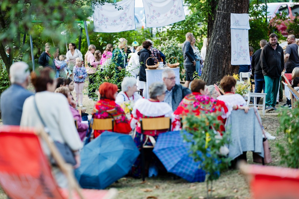 Widok ogólny, w tyle osoby z stoją i przechadzają się po ternie, część osób siedzi przy stole. Rozłożone parasolki.