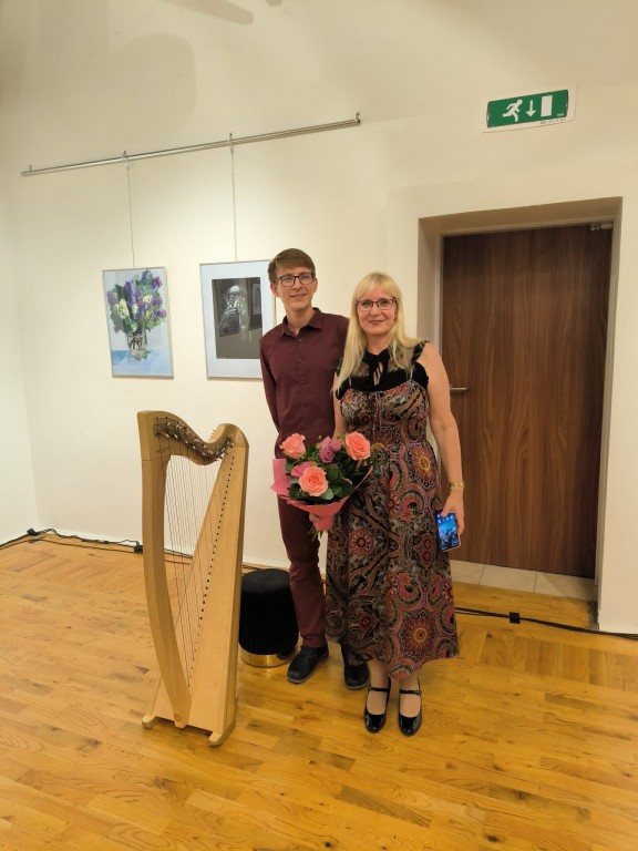 Kobieta i mężczyzna pozują z kwiatami przy harfie.