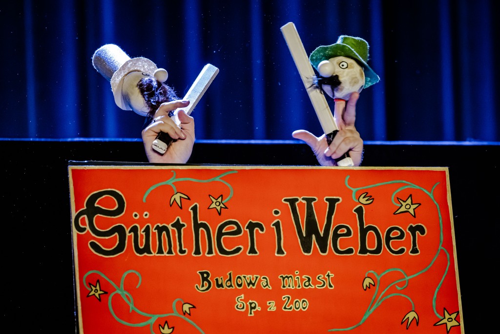 sytuacja sceniczna, nad szyldem dwie pacynki ze sobą walczą