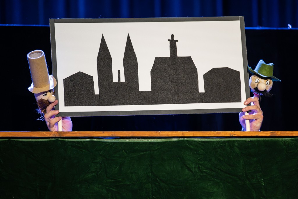 dwie pacynki trzymają tabliczkę z miastem, sytuacja scenicza