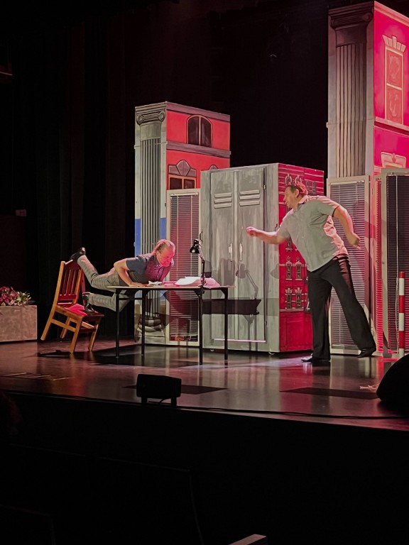 sytyuacja sceniczna, mężczyzna huśta się na krześle i opiera na stole.