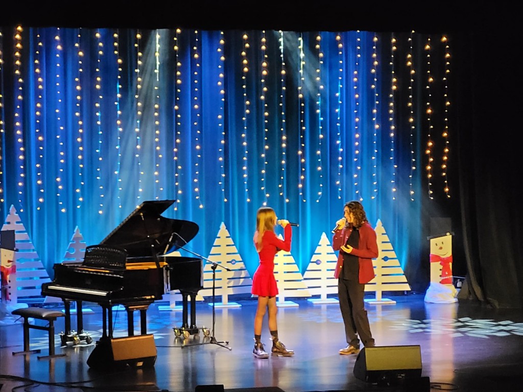 Występ sceniczny, widok z boku, na scenie duet wokalistów i fortepian.
