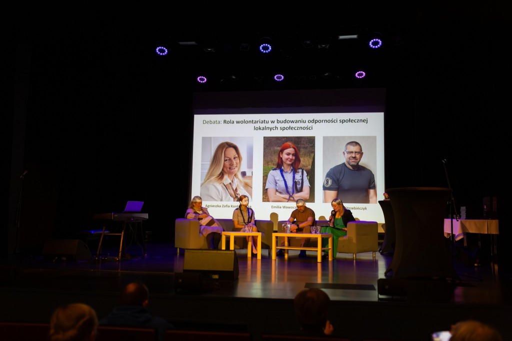 sytuacja sceniczna, 4 osoby podczas panelu. Siedzą na kanapach w tle prezentacja.