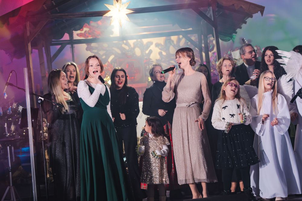 Sytuacja sceniczna, liczna grupa osób w różnym wieku podczas wykonywania utworu, śpiewają.