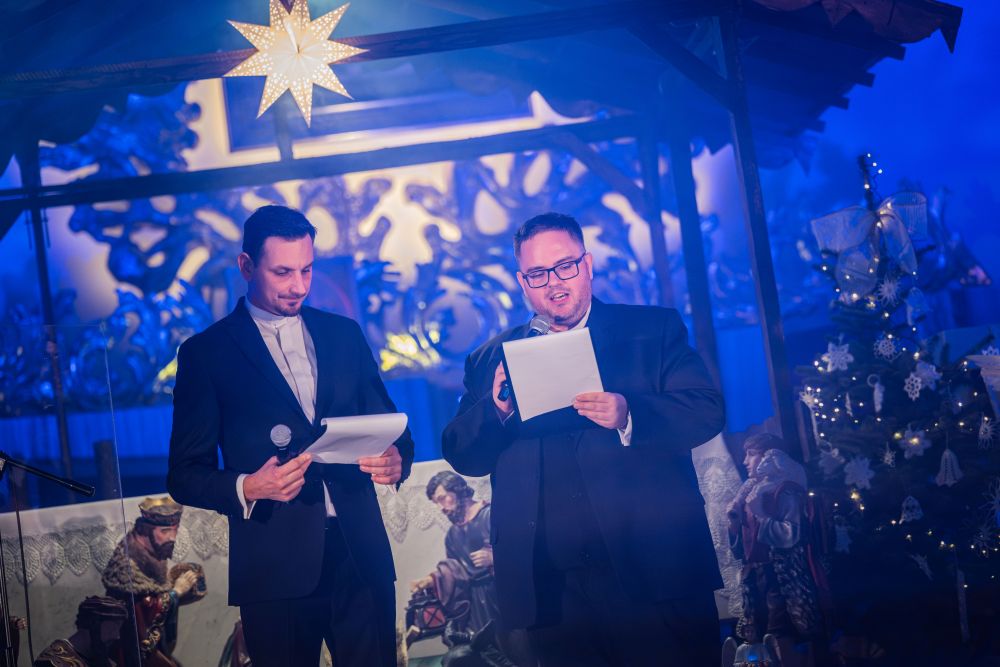 Dwóch mężczyzn z mikrofonami, jeden czyta tekst, drugi zerka w notatki.