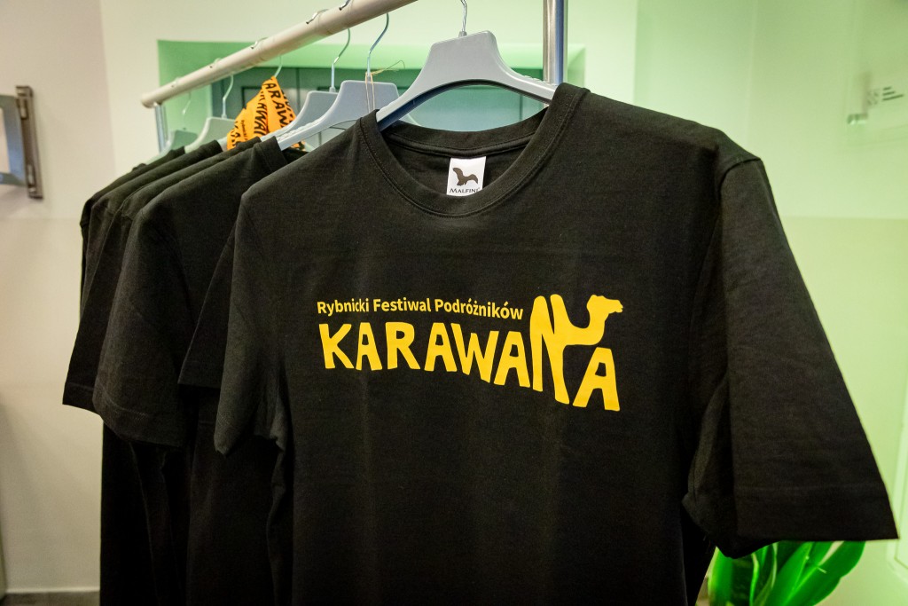Czarne koszulki z logiem “Karawana” wiszące na wieszaku.