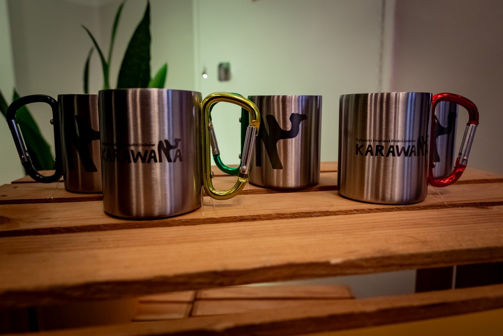 Kubki termiczne z wygrawerowaną grafiką loga “Karawana” stojące na drewnianej skrzyni.