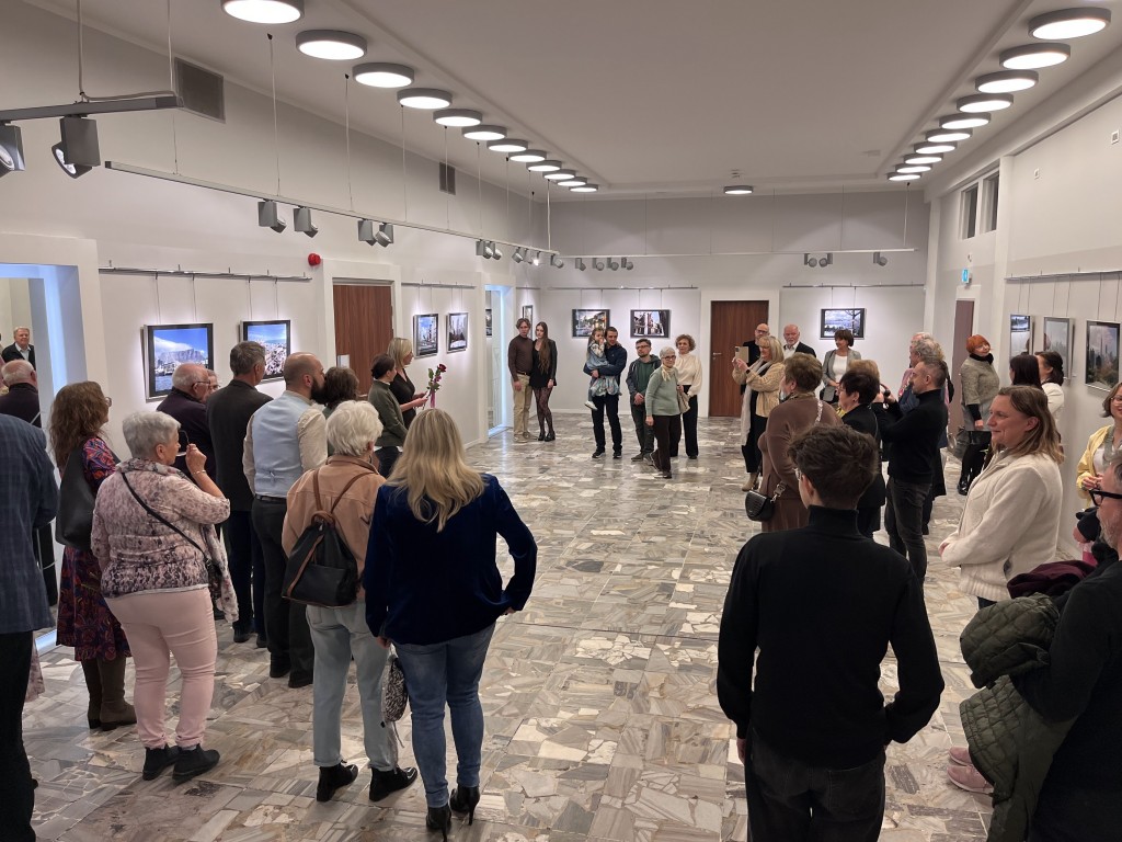 w holu, grupa osób patrzy na dwie kobiety, na ścianach wiszą fotografie
